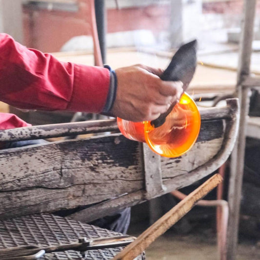 Artisan crafting bespoke glassware by shaping glowing orange mouthblown glass in workshop