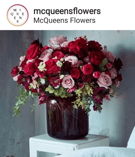 Elegant bouquet of red and pink roses in a dark glass vase by mcqueens flowers on a white table