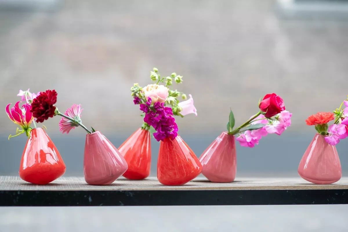 Lowlands Design tumbling vase collection in red and pink holding vibrant fresh flowers on a shelf