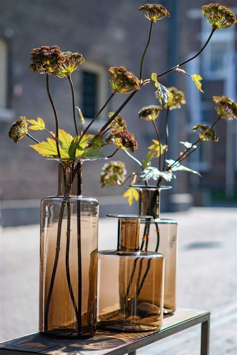 Lowlands Design bottle vase set in amber glass holding dried flowers on outdoor table