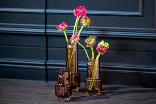 Lowlands Design brown glass vase set with pink flowers on dark wooden surface