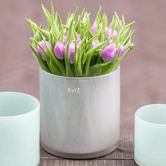 Lowlands Design cylinder vase with pink tulips and green leaves on a wooden surface