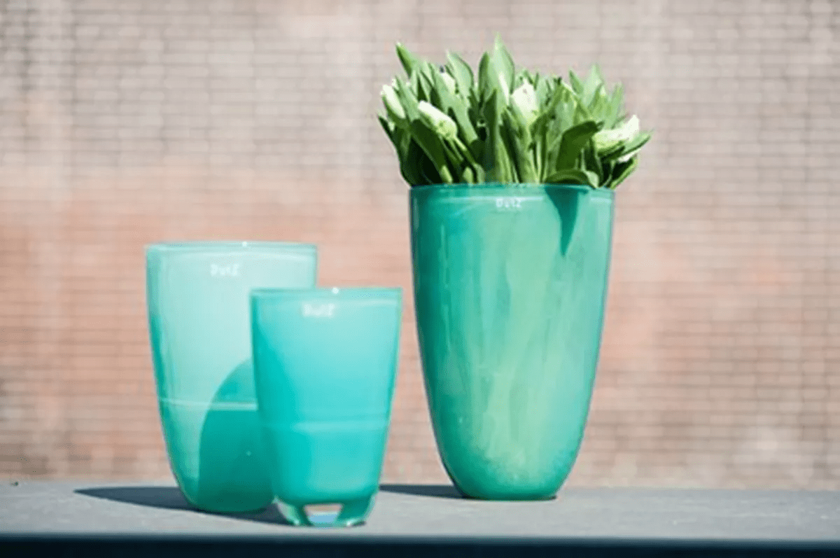 Lowlands Design turquoise ceramic flowervase with green leafy stems on table in natural light
