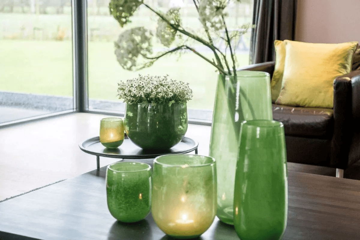 Collection of green decorative glass vases by Lowlands Design displayed on wooden table and tray