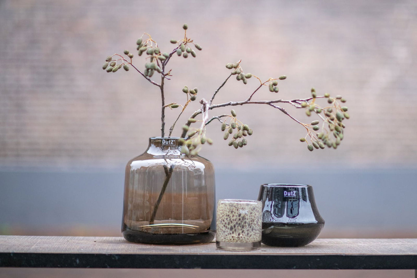 Lowlands Design orchid pot with translucent brown glass holding a branch beside two smaller decorative glass pots