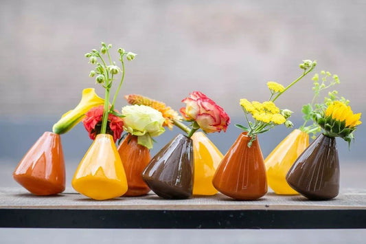 Lowlands Design tumbling vase collection in brown and yellow glass with flowers on wooden surface