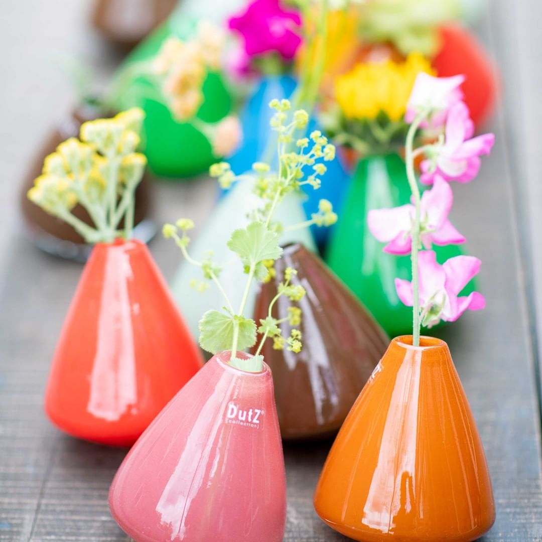 Colorful ceramic tumbling vase collection by Lowlands Design with fresh flowers on wooden surface