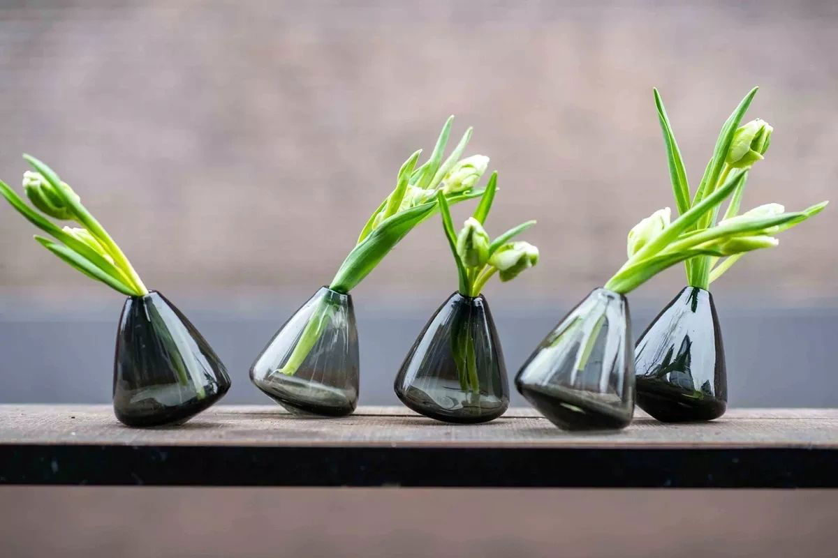 Lowlands Design tumbling vase set of five black glass vases with green flower stems on wooden surface