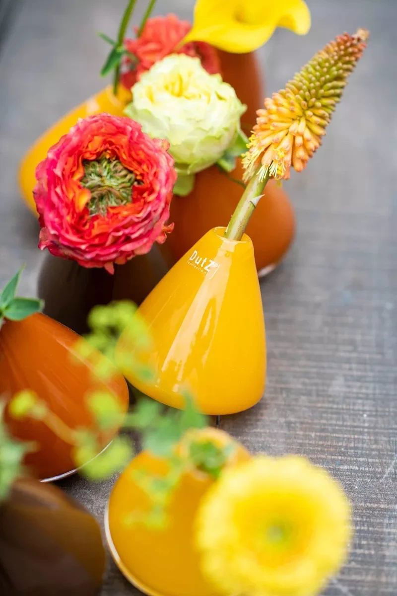 Lowlands Design tumbling vase in yellow and brown holding vibrant colourful flowers on a grey surface