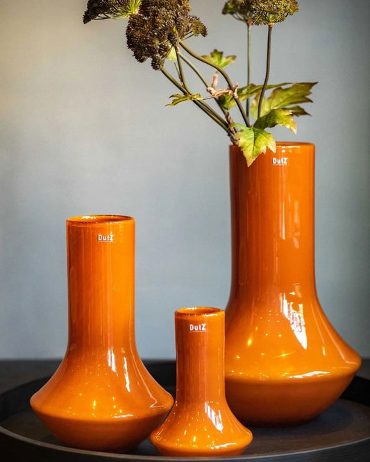 Set of three orange glass vases by Lowlands Design with glossy finish and dried flowers in one vase