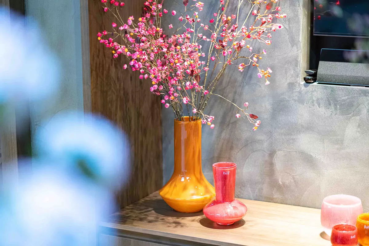 Lowlands Design orange vase with pink flowers on wooden surface next to small decorative glass pieces