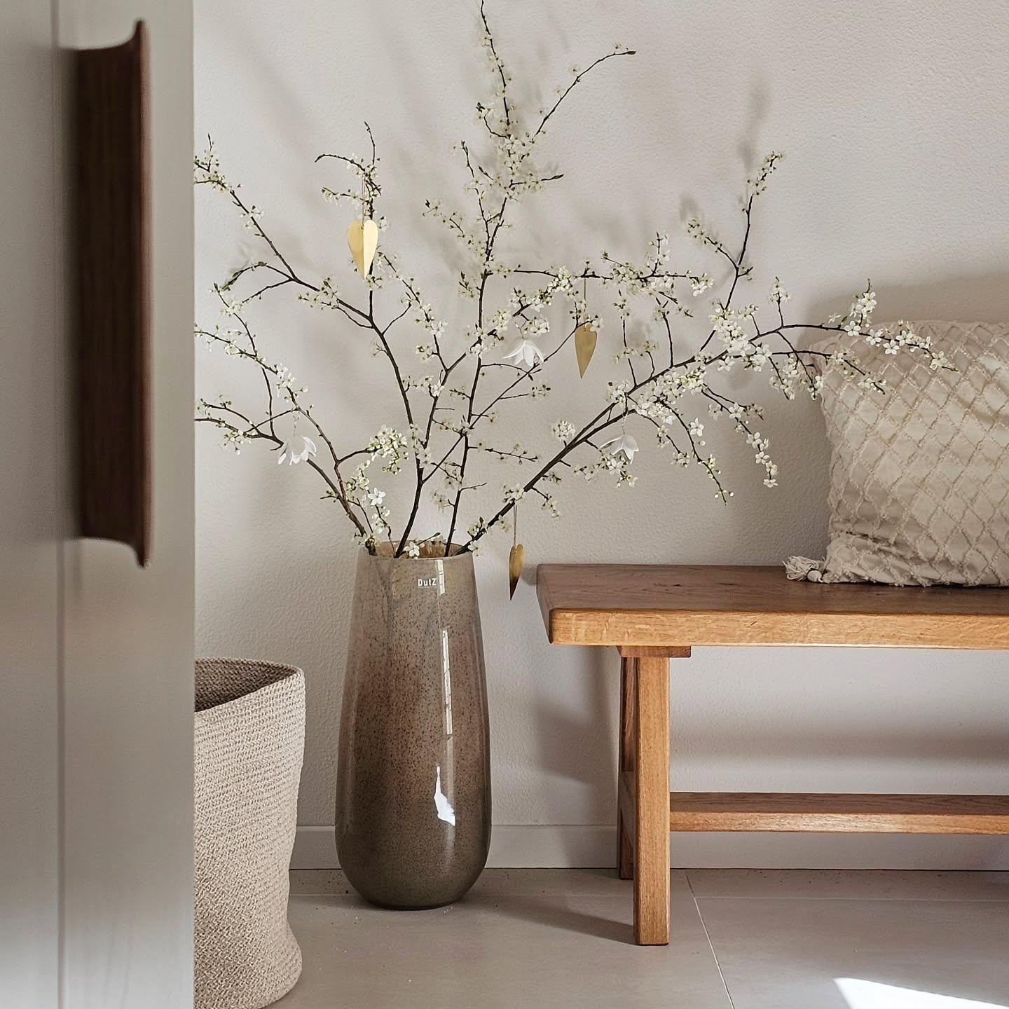 Lowlands Design tall brown ceramic vase flower with delicate white blossoms displayed next to wooden bench