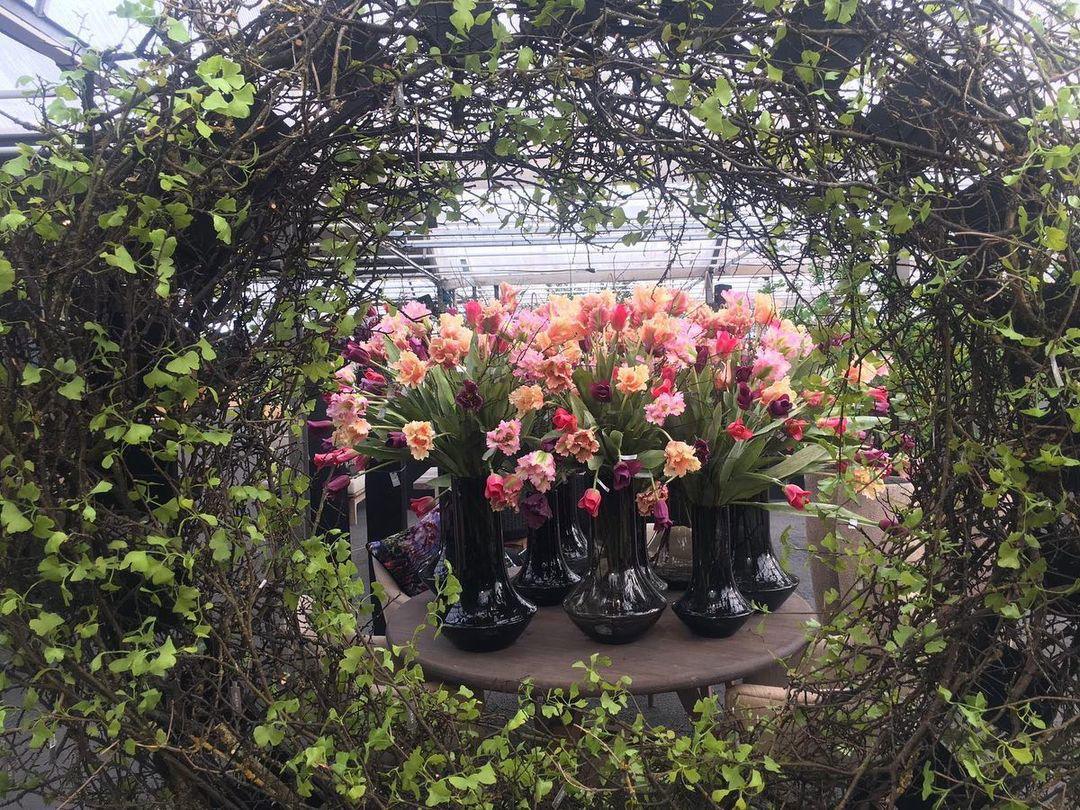 Lowlands Design black vase glass holding pink and orange flowers on a round wooden table