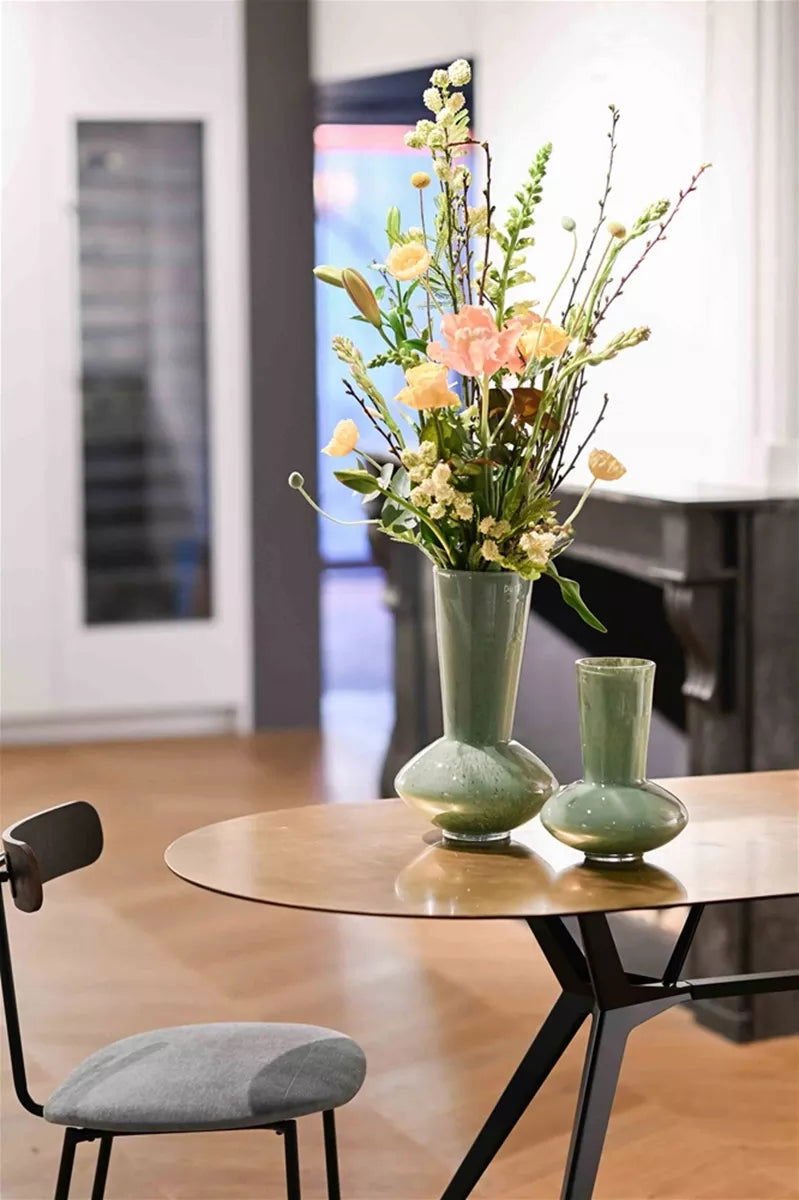 Green ceramic vase by Lowlands Design with fresh flowers on a wooden table in a modern room