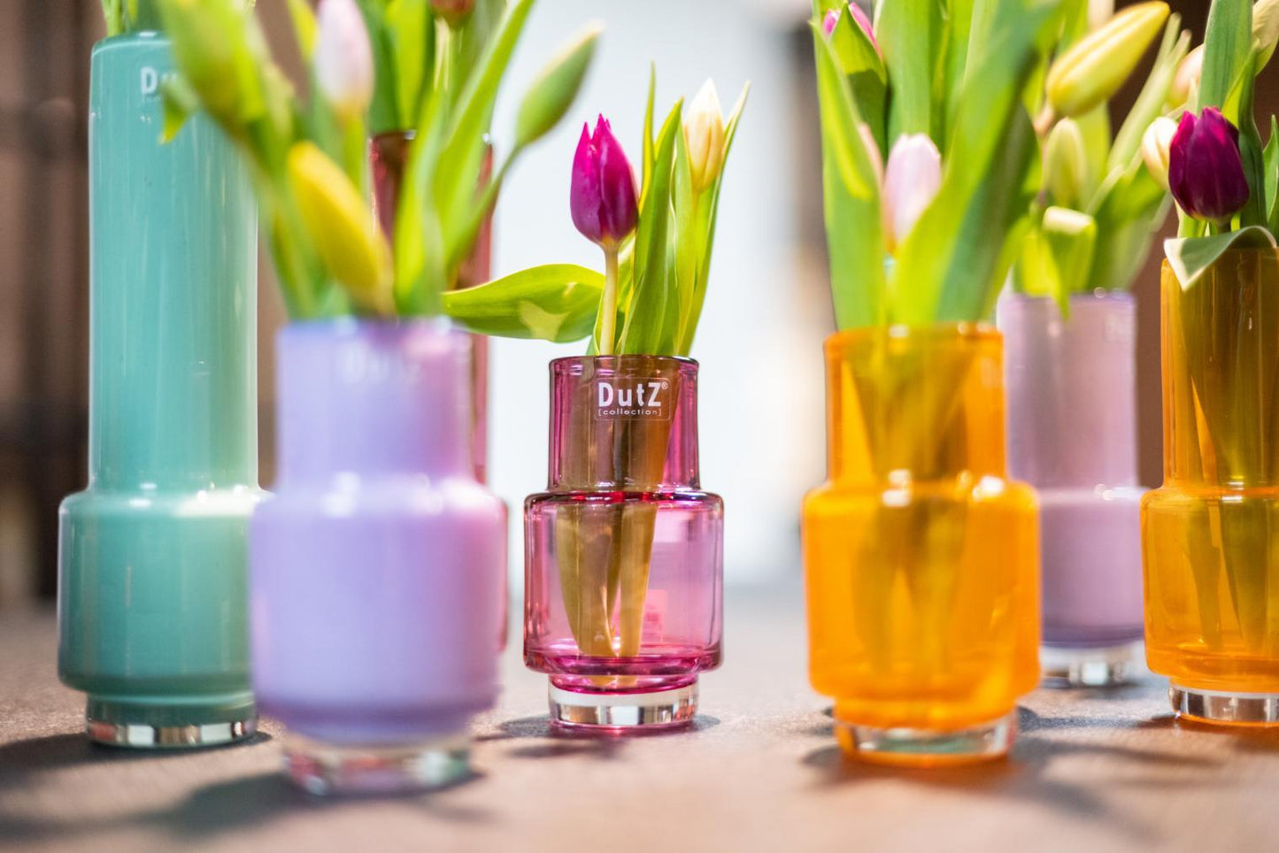 Colorful glass vase collection by Lowlands Design holding fresh tulips and green leaves