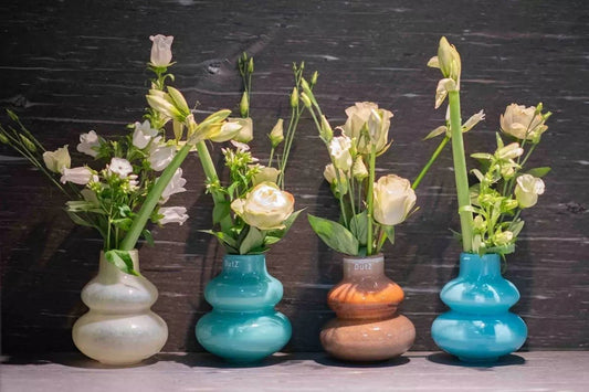 Four colourful Lowlands Design vases with white and yellow flowers arranged on a surface