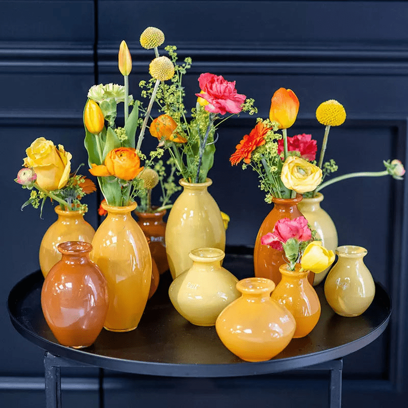 Lowlands Design ceramic vase set in various yellow and orange shades with fresh colorful flowers on black round table