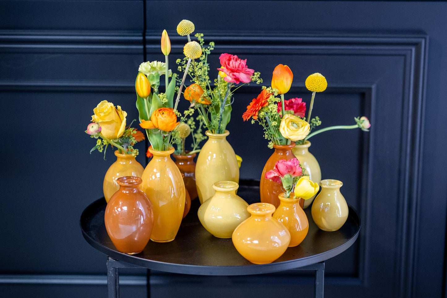 Lowlands Design vase set in yellow and orange hues with assorted flowers on a black round table