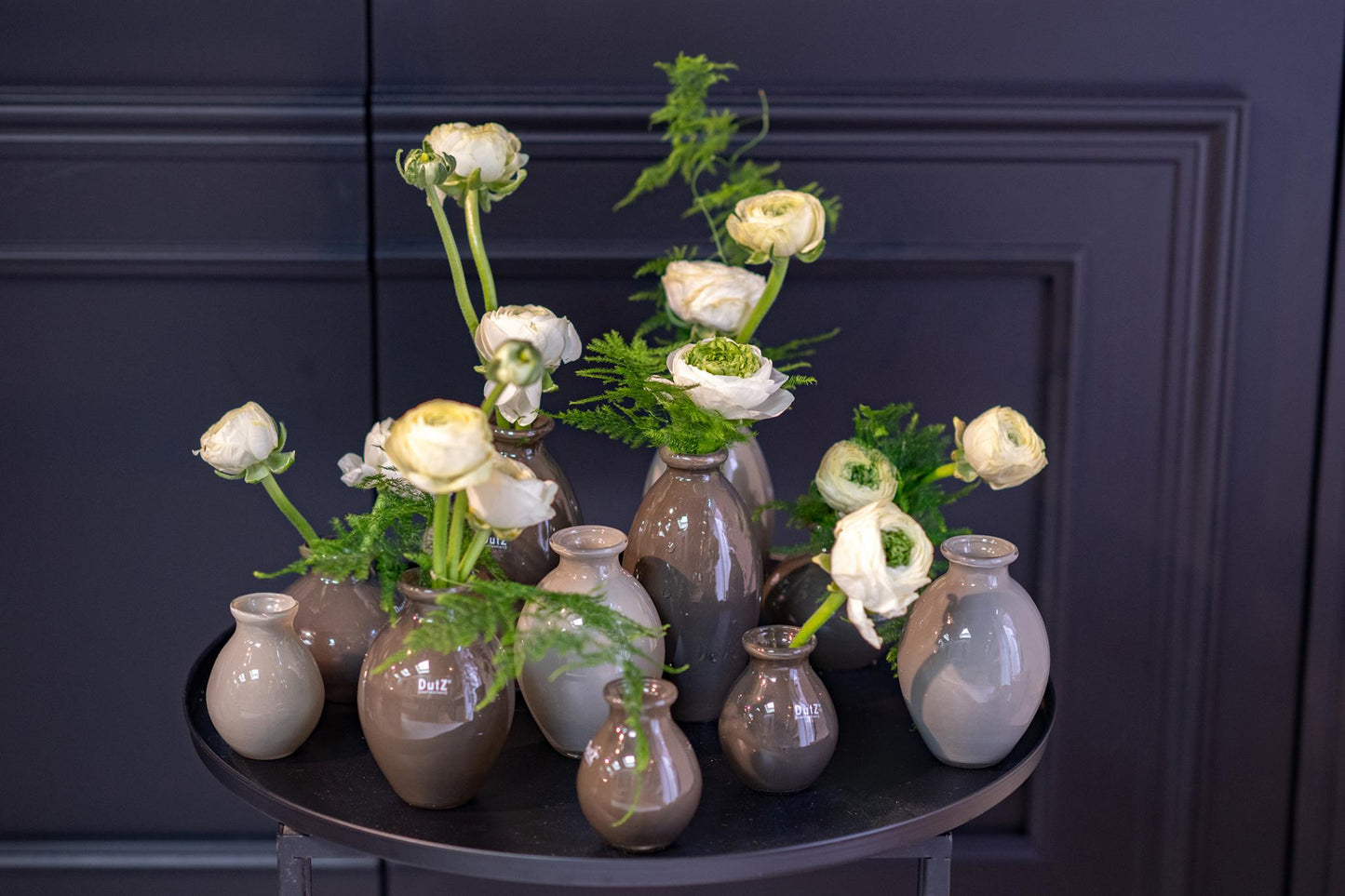 Lowlands Design gray and beige ceramic vase set with white flowers and green foliage on black table