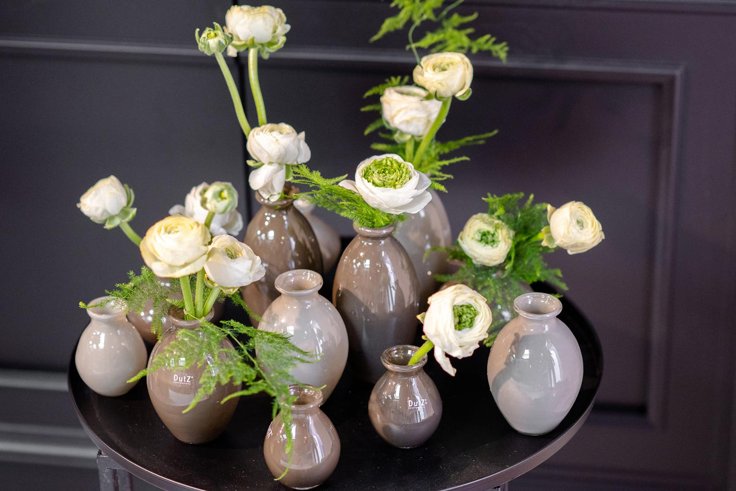 Lowlands Design ceramic vase set in neutral tones with white flowers and green foliage on a black round table