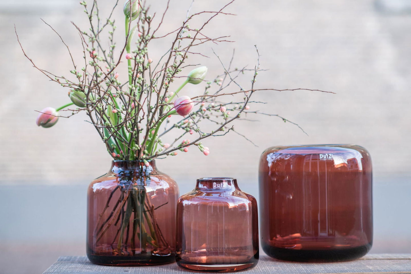 Set of three amber glass vases by Lowlands Design with one vase holding branches and flowers