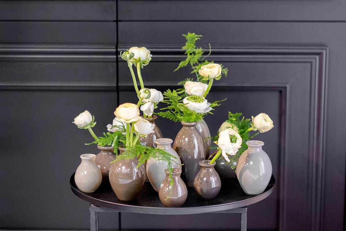 Lowlands Design ceramic vase set with neutral tones holding white flowers and greenery on a black round table