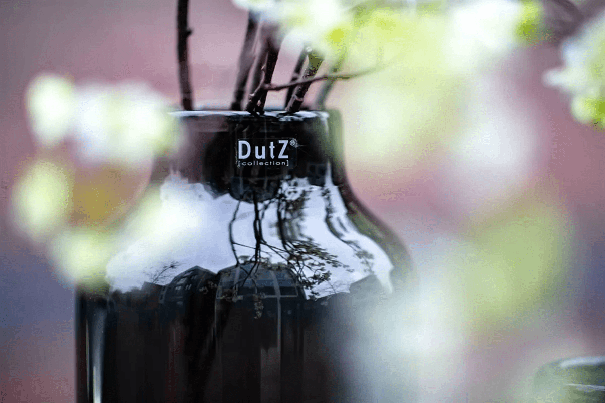 Lowlands Design black glossy DutZ collection cylinder vase with branches on blurred floral background
