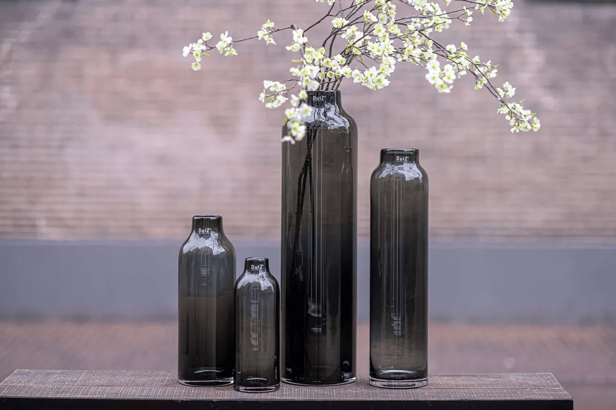 Set of four dark glass cylinders by Lowlands Design used as stylish vases with white flowers