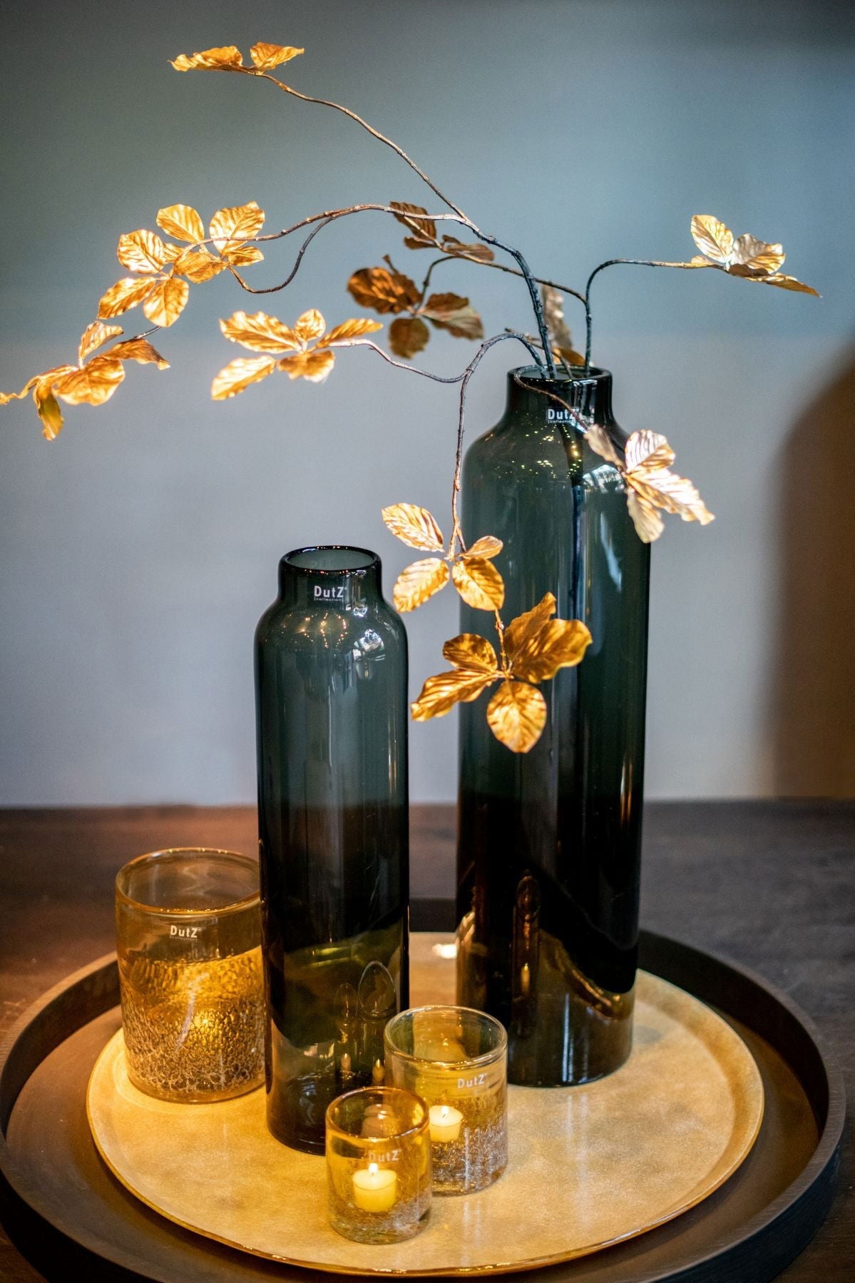 Lowlands Design dark glass cylindrical vase with decorative golden leaves on a round tray