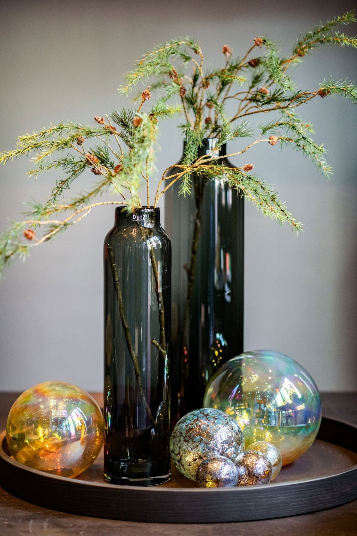 Lowlands Design tall black glass cylinders styled as vases with green leafy branches on a black tray