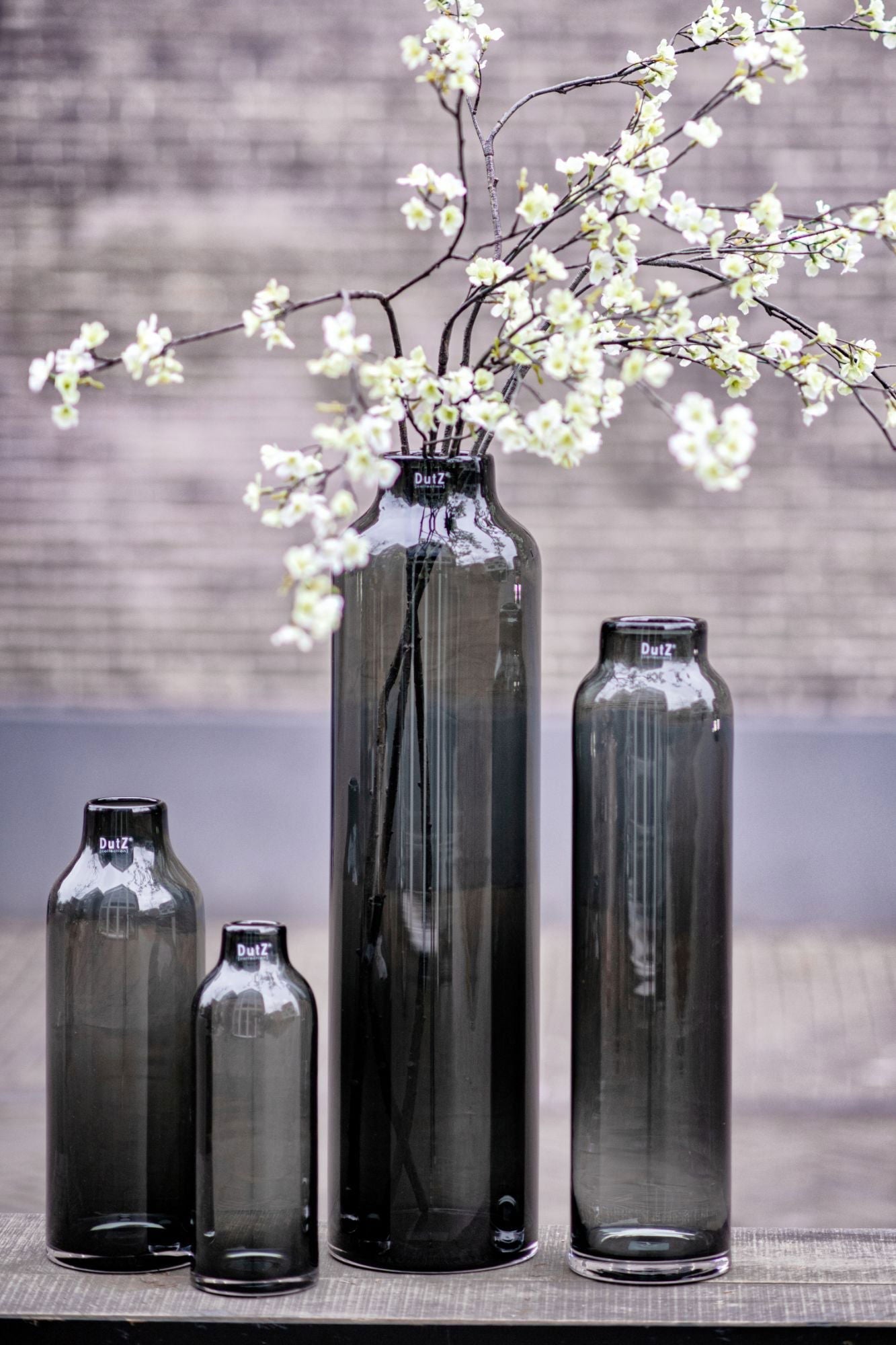 Lowlands Design cylindrical glass vase set with tall dark grey vases, one holding white blossoming branches