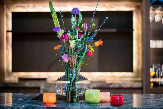Lowlands Design recycled glass vase with colorful fresh flowers on a marble table surrounded by decorative candles