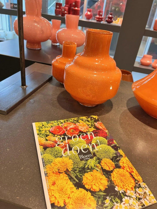 Bright orange dutz vases displayed on a dark surface next to a vibrant floral book