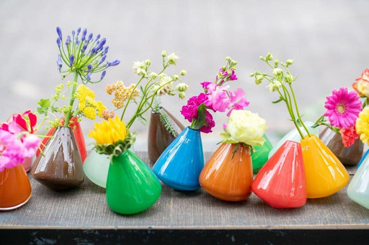 Colourful small glass vases with flowers that tumble and wobble on a wooden surface