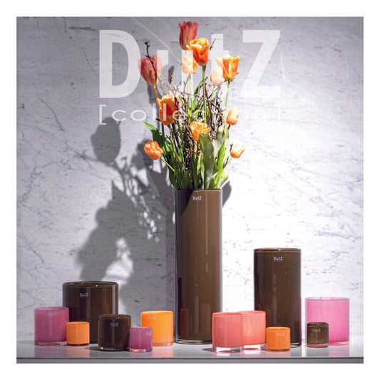 Dutz collection featuring tall brown glass vases with vibrant orange and pink flowers and matching coloured glass holders