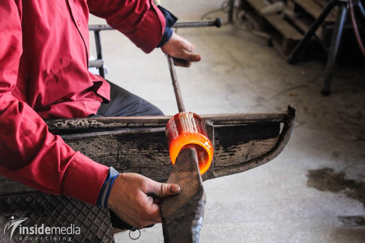 Craftsman shaping glowing mouth blown glass using traditional tools in artisan workshop