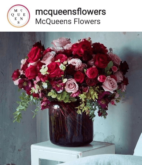 Elegant bouquet of red and pink roses in a dark glass vase by mcqueens flowers on a white table