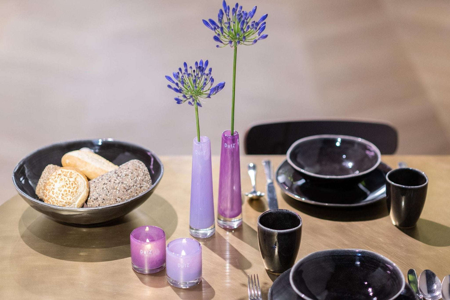 Lowlands Design solifleur vase in purple holding flowers on a dining table with black dishes and candles