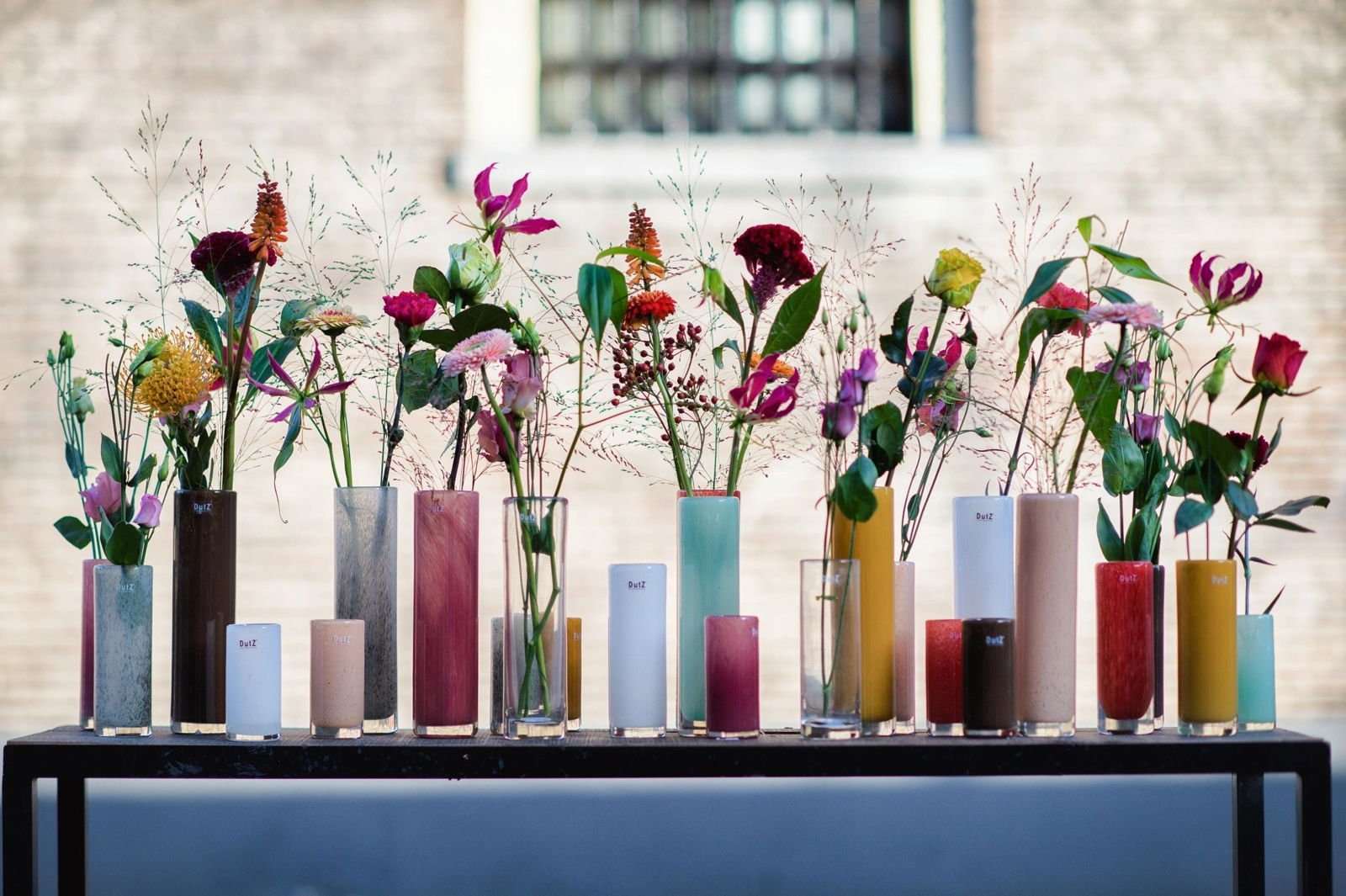 Collection of colourful cylinder vase designs by Lowlands Design holding various flowers on a black table