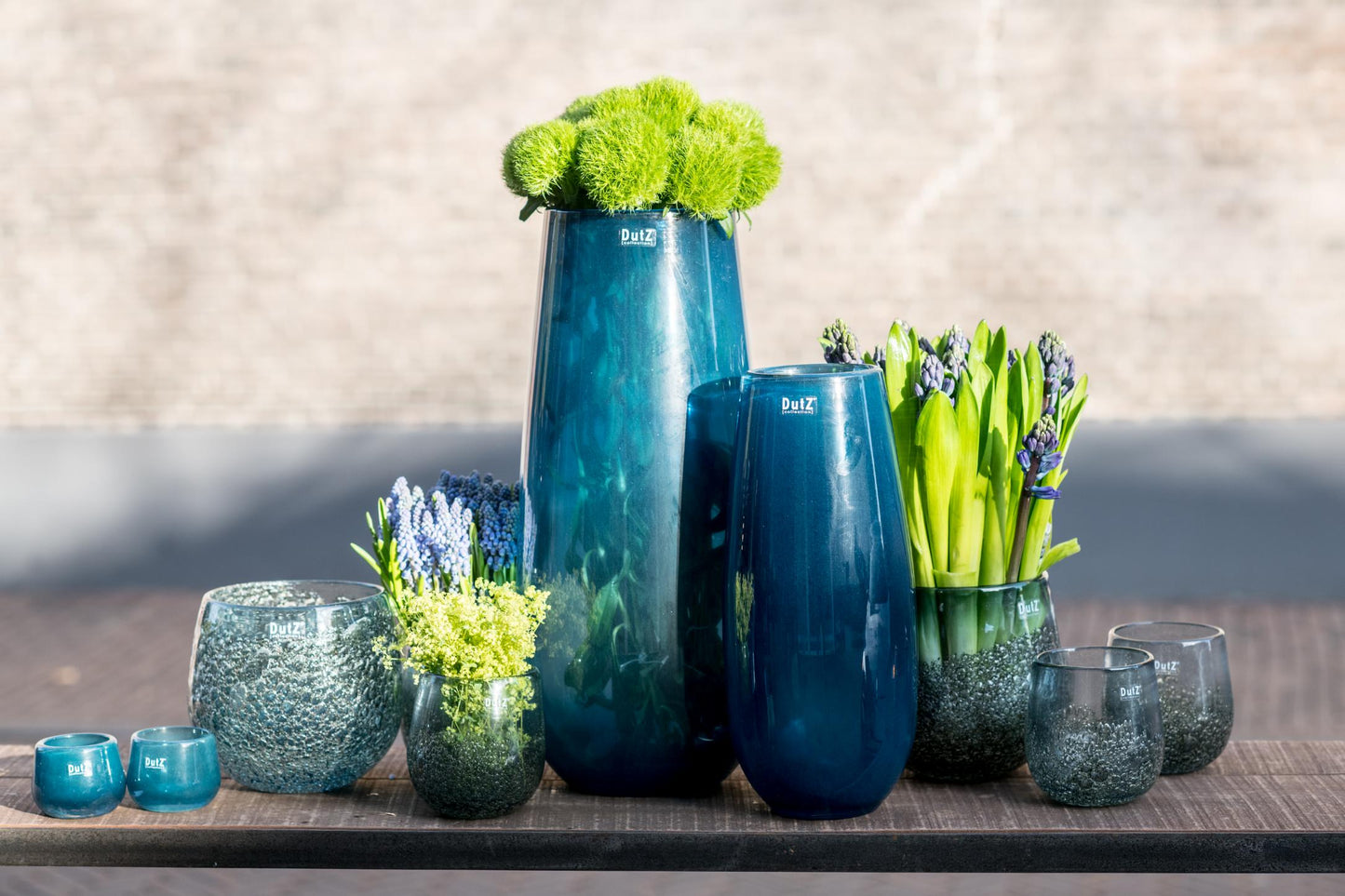 Collection of Lowlands Design glass flower vases in various sizes and shapes, featuring vibrant flowers
