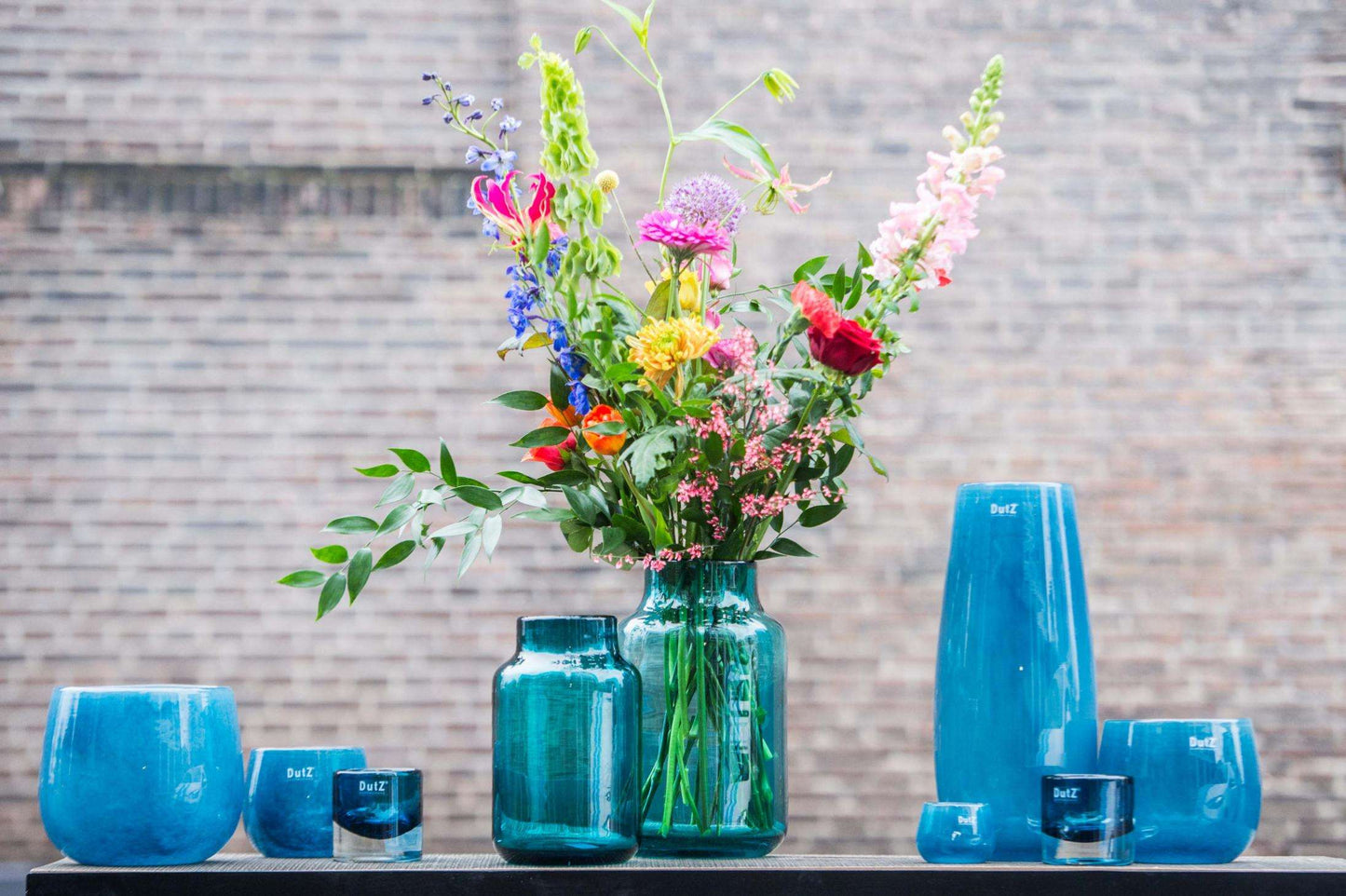 Lowlands Design glass flower vase with vibrant arrangement of colourful flowers in a stunning blue setting