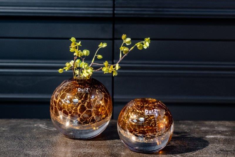 Lowlands Design brown glass ball vase with crackle effect holding yellow flower stems on dark surface