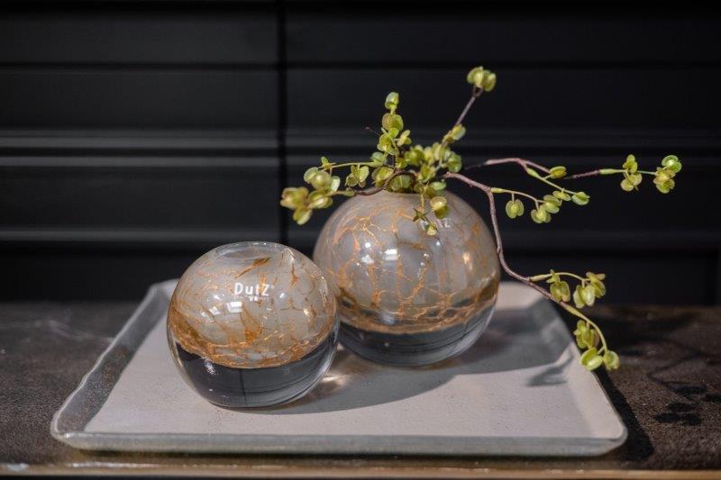 Lowlands Design glass ball vase set with decorative golden veining on a grey tray with green branches