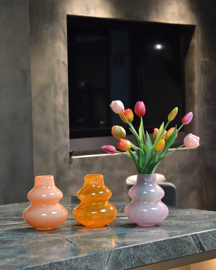 Lowlands Design beige decorative vase and two orange glass vases with tulips arranged on marble worktop