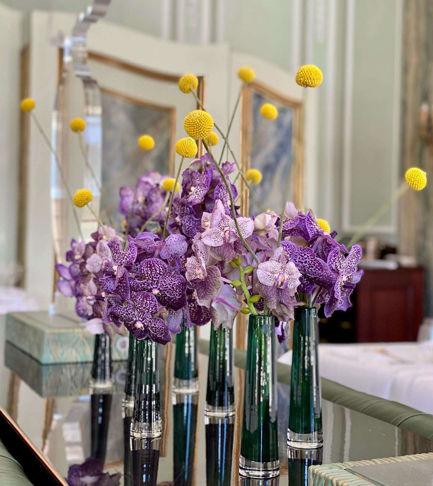 Lowlands Design solifleur budvase holding purple orchids and yellow billy ball flowers on a reflective surface