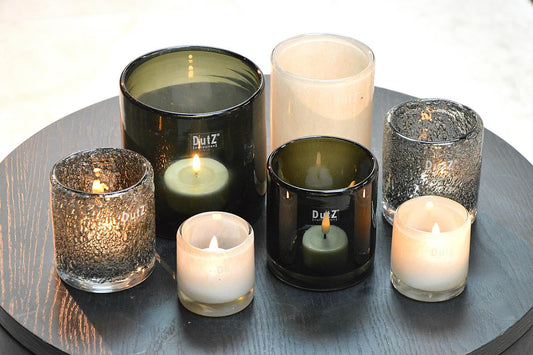 Various glass cylinder candleholders in smoke tones, displaying lit candles for elegant decor