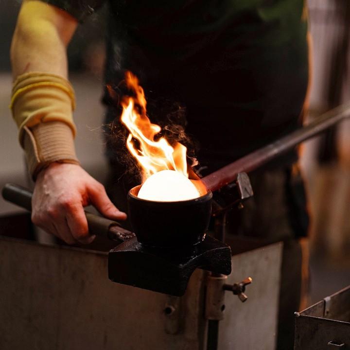 Artisan shaping glass flowervase mouthblown in a workshop with flames