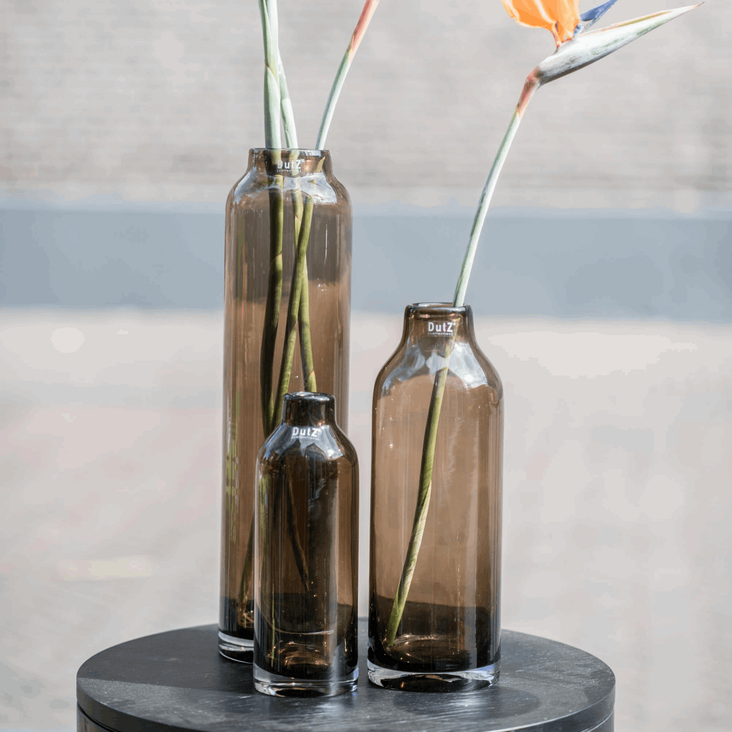 Three Lowlands Design glass vases in brown, varying sizes, perfect for displaying flowers.