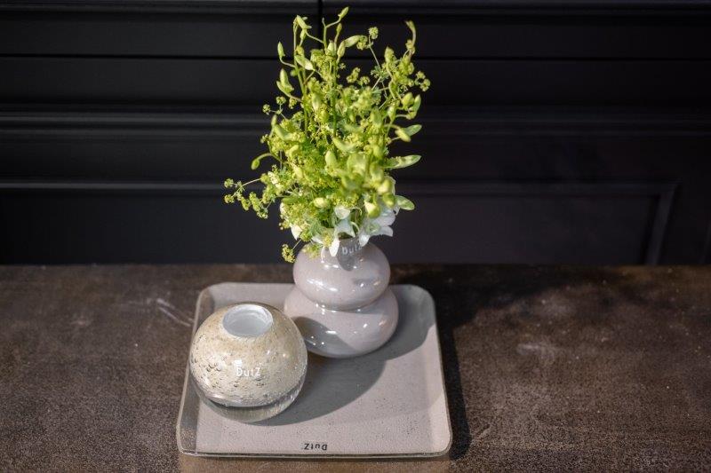 Lowlands Design tabletop display with green foliage in stacked pale ceramic vase and round pot on tray green glass vase decorative