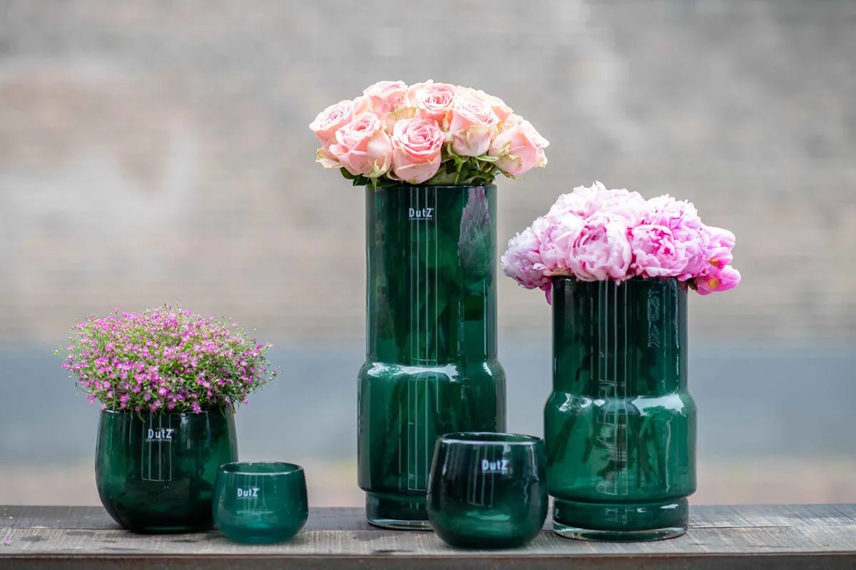 Lowlands Design green glass vase collection with various sizes holding pink flowers on wooden surface